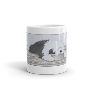May include: White ceramic mug with a black and white illustration of an Old English Sheepdog laying down and eating from a bowl. The text "Copyright 1999 Anastasia P. Bunte - All Rights Reserved" is at the bottom of the image.