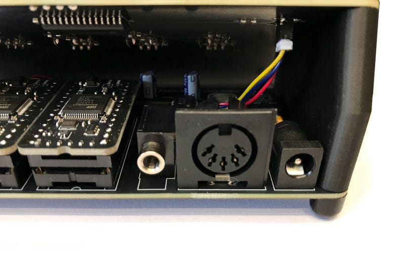 K&ouml;nnte beinhalten: Nahaufnahme des Inneren eines elektronischen Ger&auml;ts. Das Bild zeigt Leiterplatten, einen runden MIDI-Anschluss, einen Stromeingang und eine Audiobuchse. Gelbe, rote und blaue Dr&auml;hte sind sichtbar.