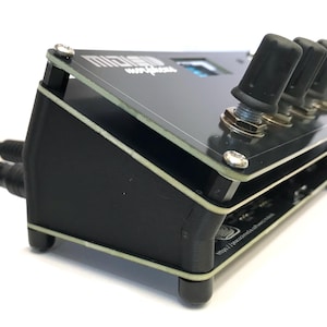 K&ouml;nnte beinhalten: Schwarzes elektronisches Ger&auml;t mit klarer Oberseite und vier schwarzen Kn&ouml;pfen. Das Ger&auml;t hat einen kleinen Bildschirm und mehrere Anschl&uuml;sse. Der Text "MIDI SUN" ist oben sichtbar. Zwei schwarze Kabel sind an der Seite angeschlossen.