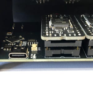 K&ouml;nnte beinhalten: Nahaufnahme eines schwarzen elektronischen Ger&auml;ts mit einem USB-C-Anschluss und zwei Leiterplatten. Die Leiterplatten sind gestapelt und haben mehrere kleine Komponenten. Das Ger&auml;t befindet sich auf einer wei&szlig;en Oberfl&auml;che.