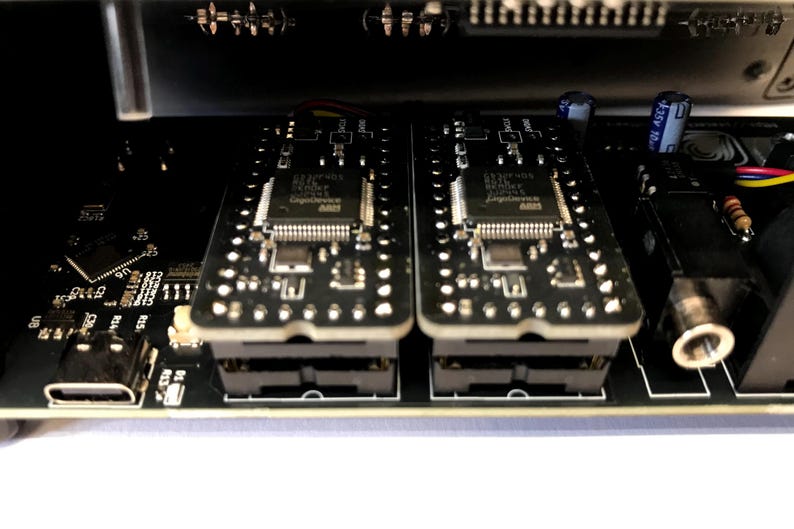 K&ouml;nnte beinhalten: Nahaufnahme von elektronischen Bauteilen, darunter zwei schwarze Leiterplatten mit integrierten Schaltkreisen und Stiften. Die Platinen sind in einem schwarzen Geh&auml;use montiert, mit einem USB-Anschluss und Kondensatoren.