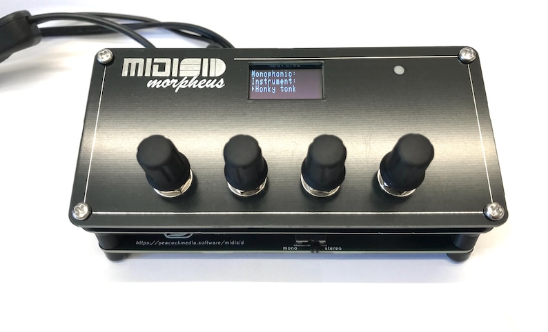 K&ouml;nnte beinhalten: Schwarzer elektronischer Musiksynthesizer mit dem Text "MIDIGID morpheus" und einem kleinen Bildschirm, der Optionen anzeigt. Er hat vier schwarze Kn&ouml;pfe und eine silberne Zierleiste. Ein Kabel ist oben links angeschlossen.