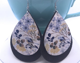 May include: A pair of teardrop-shaped earrings with a floral and bird print on a white background. The earrings are layered with a black suede backing.