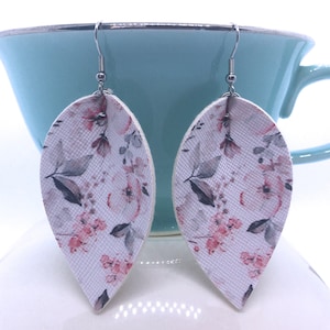 May include: A pair of white teardrop-shaped earrings with a pink and gray floral pattern.