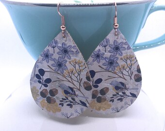 May include: A pair of teardrop-shaped earrings with a white background and a floral pattern in shades of blue, yellow, and brown. The earrings have a rose gold hook.