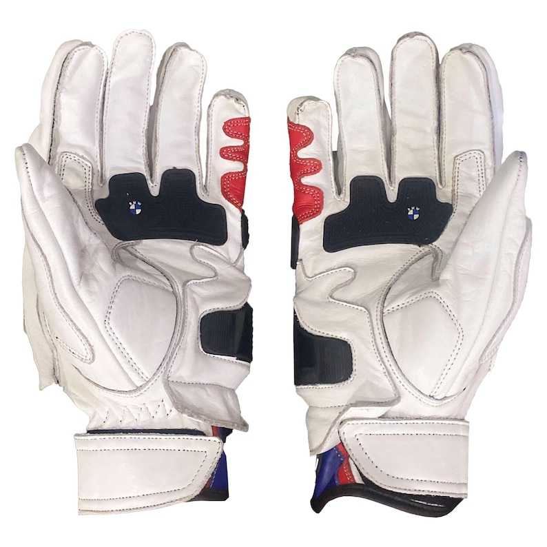 May include: White leather motorcycle gloves with black and red accents. The gloves feature a padded design with a BMW logo on the knuckles and wrist straps. The gloves have a secure wrist closure.