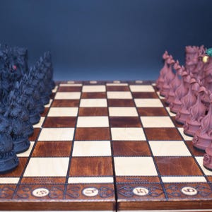 May include: A detailed shot of a chess set with intricately designed pieces. The black pieces have a dragon-like appearance, while the opposing pieces are a reddish-brown color. The chessboard is made of wood with a checkered pattern.