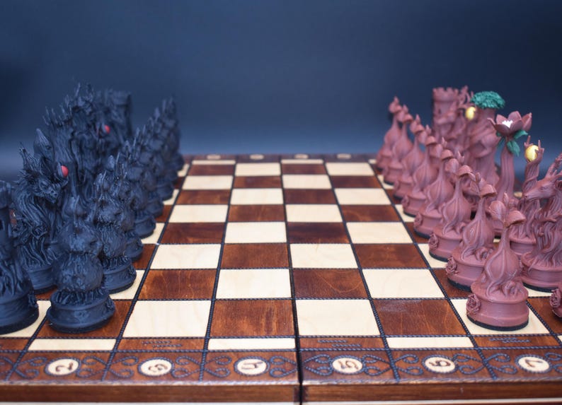 May include: A detailed shot of a chess set with intricately designed pieces. The black pieces have a dragon-like appearance, while the opposing pieces are a reddish-brown color. The chessboard is made of wood with a checkered pattern.