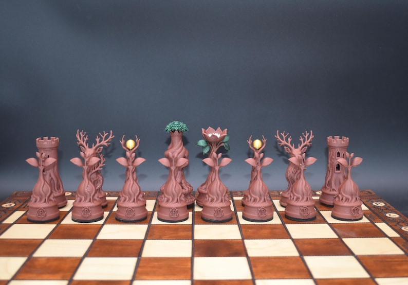 May include: A unique chess set with pieces designed to resemble trees and forest elements. The pieces are a reddish-brown color and include rooks, deer, and pieces with glowing or leafy tops. The set is displayed on a wooden chessboard.