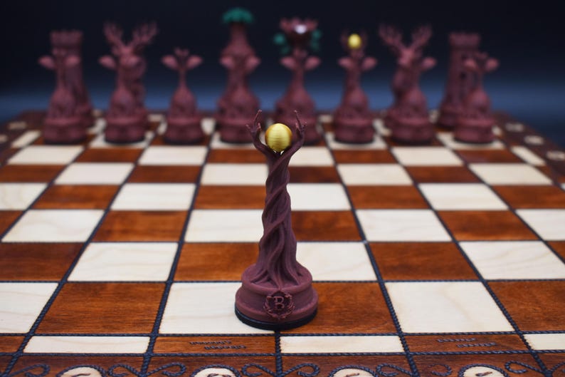 May include: A unique chess set featuring intricately designed pieces. The pieces are a deep burgundy color, with some pieces resembling trees and others with deer antlers. The board is made of wood with a checkerboard pattern.