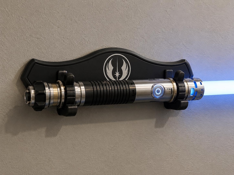 K&ouml;nnte beinhalten: Ein Lichtschwert mit silbernem und schwarzem Griff, das eine hellblaue Klinge aussendet. Das Lichtschwert ist auf einer schwarzen Wandplakette mit einem wei&szlig;en Emblem montiert. Es ist ein Requisit aus dem Star Wars-Franchise.