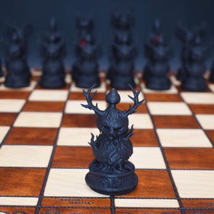 May include: A black chess set with intricately designed pieces on a wooden chessboard. The focal point is a detailed black chess piece with antlers, flames, and a skull-like face. The board has alternating light and dark squares.