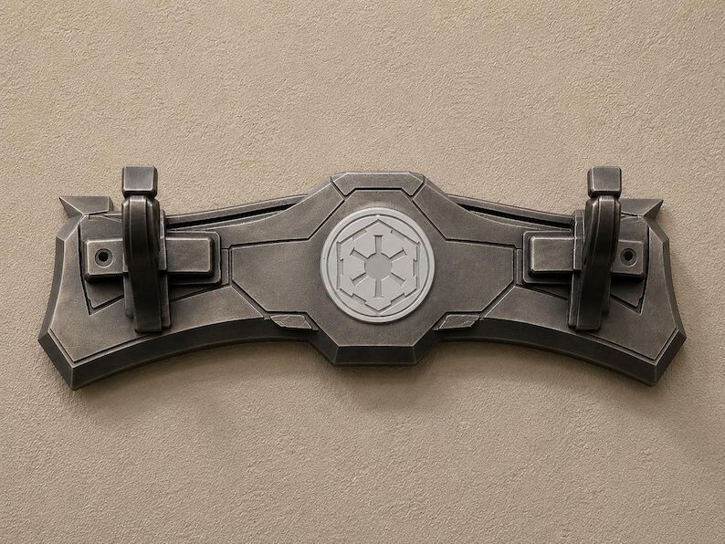 K&ouml;nnte beinhalten: Ein dunkelgrauer, an der Wand montierter Kleiderhaken mit zwei Haken und einem zentralen Emblem. Der Haken hat ein geometrisches Design mit einem erhabenen, kreisf&ouml;rmigen Emblem in der Mitte. Die Haken sind schwarz und rechteckig. Der Haken ist aus einem haltbaren Material.