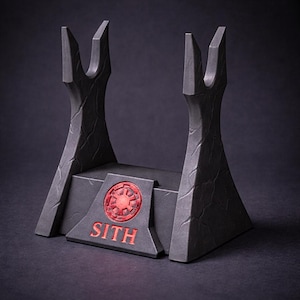 May include: A black lightsaber display stand with a red Sith emblem and text. The stand has a textured surface and two upright supports with a notched design. The base is rectangular with angled sides.
