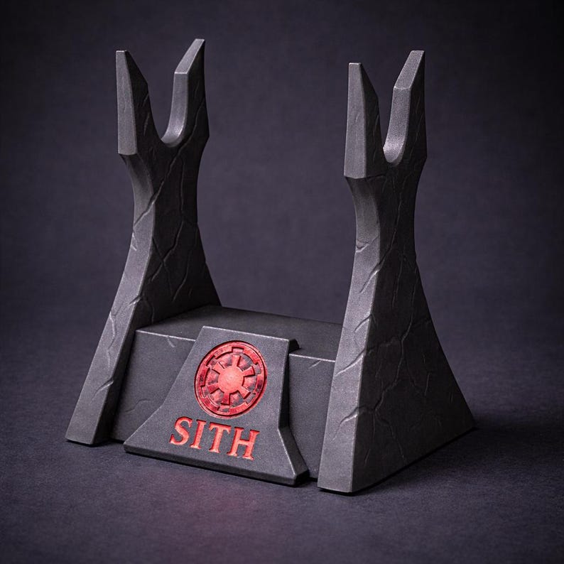 May include: A black lightsaber display stand with a red Sith emblem and text. The stand has a textured surface and two upright supports with a notched design. The base is rectangular with angled sides.