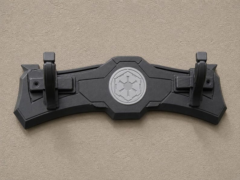 K&ouml;nnte beinhalten: Ein schwarzer, an der Wand montierter Displayst&auml;nder mit zwei Haken. Der St&auml;nder hat ein zentrales Emblem und ist f&uuml;r die Aufnahme eines Lichtschwerts konzipiert. Der St&auml;nder besteht aus einem haltbaren Material und ist f&uuml;r die Wandmontage konzipiert.