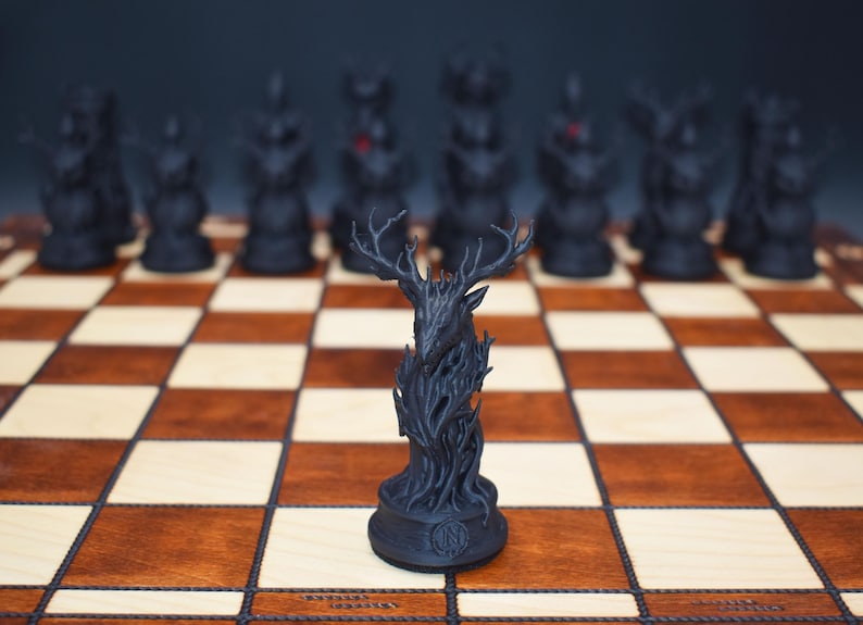 May include: A black chess set with a unique design. The chess pieces are arranged on a wooden chessboard. The focal point is a stag chess piece, with other pieces in the background. The board has alternating light and dark squares.