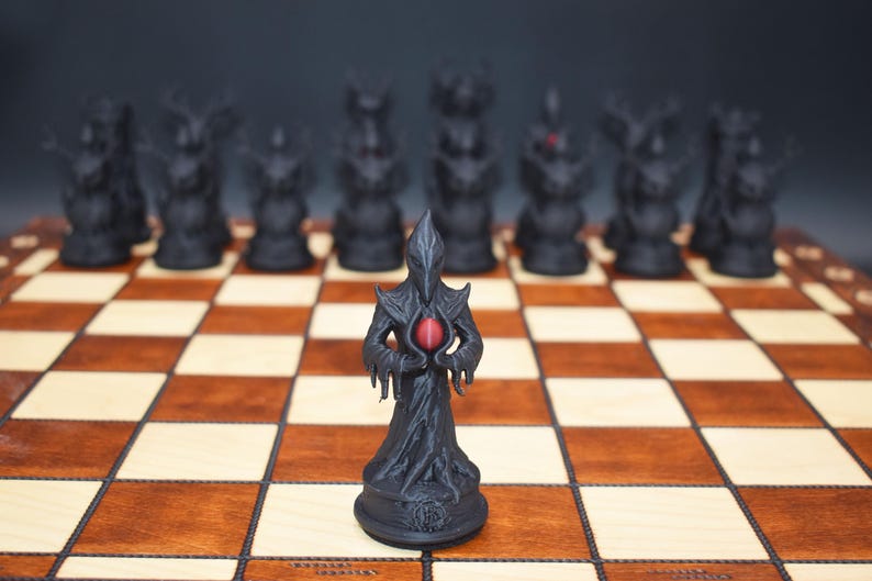 May include: A black chess set with a fantasy theme. The pieces are dark figures with intricate designs, set on a brown and beige checkered board. The central piece holds a red orb.