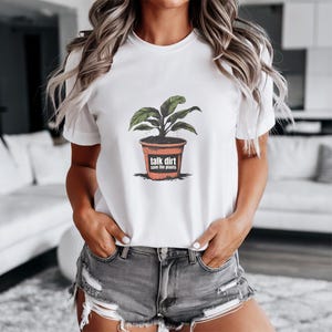 Puede incluir: Camiseta blanca con un gráfico de una planta en maceta y el texto "talk dirt save the plants".
