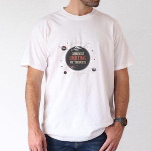 Könnte beinhalten: Weißes T-Shirt mit einem schwarzen und roten Grafikdesign, das einen Kreis mit dem Text "Currently Orbiting My Thoughts" zeigt.