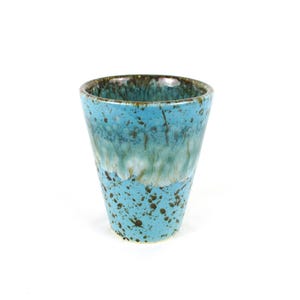 May include: A handmade ceramic tumbler with a turquoise glaze and brown speckles. The interior and rim have a darker brown color. The cup has a tapered shape and is set against a white background.