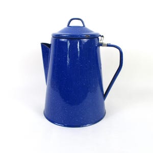 May include: A blue enamelware coffee pot with a lid and handle. The pot has a speckled pattern and a spout for pouring. The handle is a simple, curved design. The pot is likely used for camping or outdoor activities.