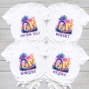 May include: White t-shirts with a colorful Ferris wheel and roller coaster design. Each shirt has a different name printed below the graphic: "CUSTOM TEXT", "ROBERT", "DARLENE", and "HELENA". The background features a watercolor-style sunset.