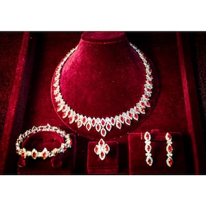Puede incluir: Un conjunto de collar, pulsera y pendientes de rubí rojo en una caja de terciopelo. Las joyas están hechas de plata y presentan piedras de rubí rojo.