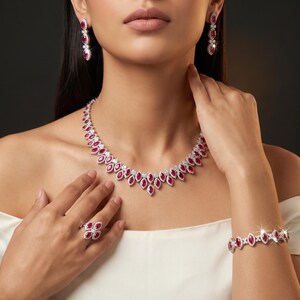 May include: A jewelry set consisting of a necklace, a bracelet, a ring, and drop earrings. Each piece features marquise-cut red gemstones surrounded by small clear stones set in a silver-toned metal, creating a cohesive floral-inspired design.