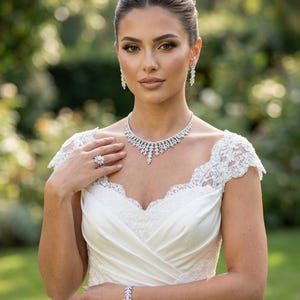 May include: A white satin dress with lace cap sleeves and a sweetheart neckline, paired with a silver-toned jewelry set featuring a necklace, drop earrings, a bracelet, and a large floral-shaped ring, all adorned with clear sparkling stones.