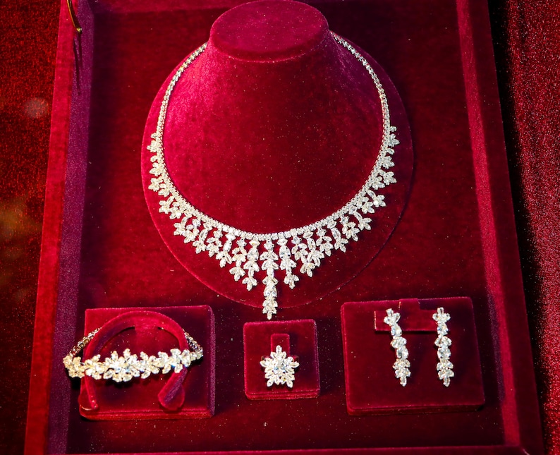May include: A diamond jewelry set displayed on a red velvet background. The set includes a necklace, a bracelet, and a pair of earrings.