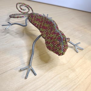 May include: A handcrafted beaded lizard sculpture. The lizard's body is covered in red and green beads, with a curled tail. The legs are made of silver wire, and the eyes are brown. This unique piece is a decorative item.