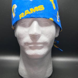 May include: Blue surgical cap with the word "RAMS" in yellow lettering. The cap also features the team's logo in yellow and white. The cap is tied at the back with blue and yellow fabric.