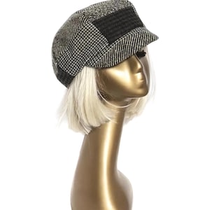 May include: A newsboy style cap with a houndstooth pattern in black and white, and a dark gray rectangular patch on the front. The cap is displayed on a gold mannequin head with short, blonde hair.