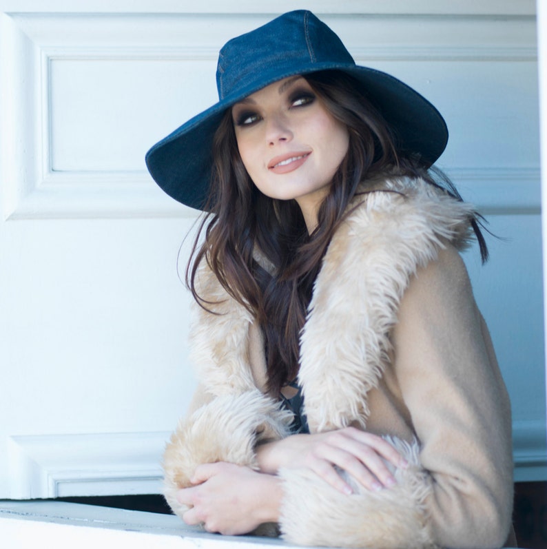 May include: A wide-brimmed denim hat and a tan coat with a faux fur collar and cuffs. The hat is a dark blue, and the coat is a neutral colour. The style suggests a bohemian or vintage aesthetic, suitable for cooler weather.