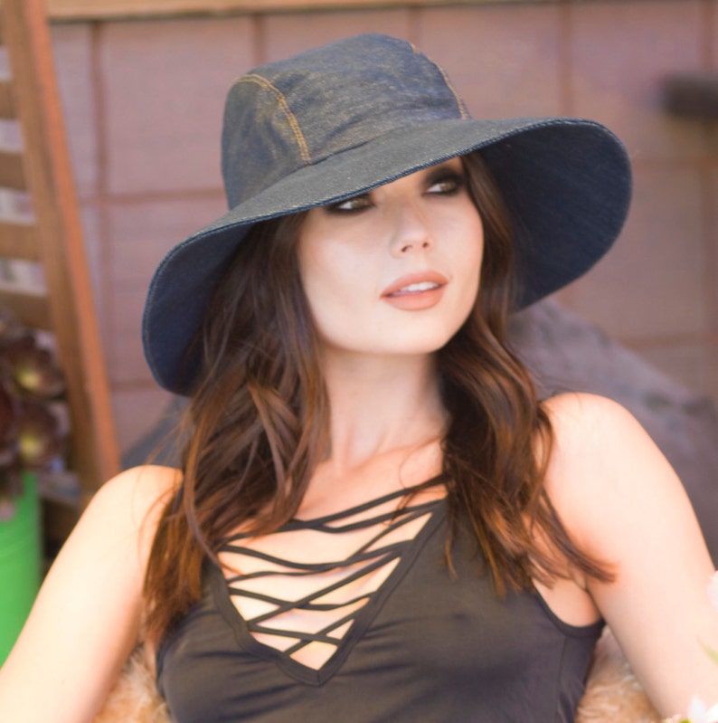 May include: A woman wearing a wide-brimmed denim hat with a black criss-cross top.