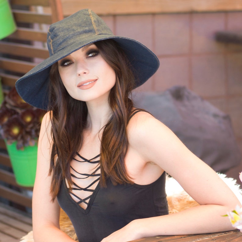 May include: A woman wearing a denim sun hat and a black sleeveless top with a criss-cross design in the front.
