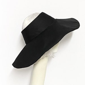 以下が含まれることがあります： 大きな平らなつばが付いた、広いつばの黒い日よけ帽子。帽子は柔らかく軽量な生地で作られており、シンプルでエレガントなデザインです。