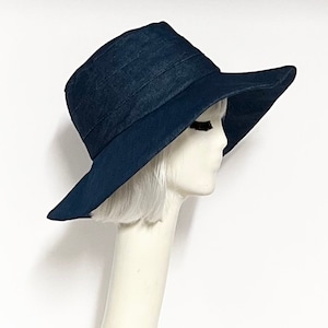 Puede incluir: Un sombrero de sol azul marino de ala ancha con un borde ligeramente curvado. El sombrero está hecho de una tela suave y texturizada.