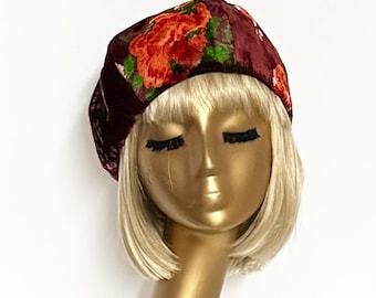 May include: A burgundy velvet beret with a floral pattern in shades of red, orange, and green.