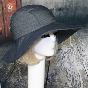 May include: A wide-brimmed black sun hat with a slightly textured fabric. The hat is worn on a white mannequin head.