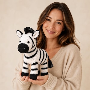 Puede incluir: Un pequeño juguete de cebra tejido a mano con un cuerpo blanco y rayas negras distintivas, un hocico negro, orejas negras y una crin negra. El animal de peluche tiene una pequeña cola negra y ojos redondos, elaborado con tejido de punto.
