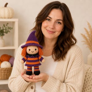May include: A knitted doll shaped like a witch, featuring a purple and orange striped dress, a matching pointed hat, and orange yarn hair. The doll has a beige face with embroidered black eyes and a small smile, wearing black shoes.