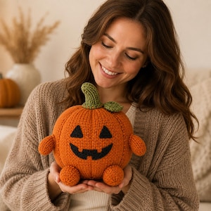 Puede incluir: Un juguete de calabaza tejido de color naranja con un tallo y una hoja verdes, que presenta una cara de jack-o'-lantern negra bordada con dos ojos triangulares y una boca dentada. La calabaza de peluche tiene dos brazos y dos pies pequeños.