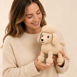 May include: A beige knitted poodle toy featuring a textured curly head, long floppy ears, and pom-pom style cuffs on its legs. The stuffed animal has embroidered black eyes, a small black nose, and a stitched mouth, crafted with a soft yarn finish.