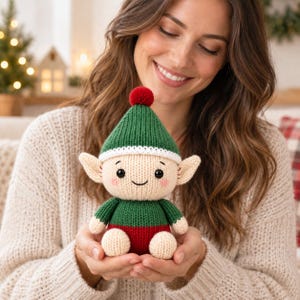Pode incluir: Uma pequena boneca elfo tricotada à mão com um gorro pontiagudo verde com um pompom vermelho, um rosto cor de creme com olhos bordados pretos e bochechas rosadas, e um corpo verde e vermelho com mãos e pés cor de creme.