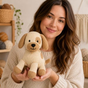 Könnte beinhalten: Ein gestricktes Stoffhund-Spielzeug mit cremefarbenem Körper sowie beigefarbenen Ohren, Pfoten und einem Fleck über einem Auge. Das Spielzeug hat eine schwarz gestickte Nase und einen Mund sowie kleine schwarze Perlenaugen aus weichem Garn.