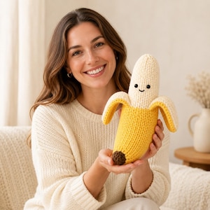 Op de afbeelding: Een gebreid bananenknuffeltje met een crèmekleurige bovenkant, een felgeel lichaam met gedeeltelijk gepelde delen en een klein bruin puntje aan de onderkant. De banaan heeft twee kleine zwarte kraaloogjes en een eenvoudig geborduurde zwarte glimlach.