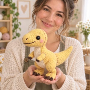 Puede incluir: Un juguete de dinosaurio tejido en color amarillo brillante con una barriga color crema. El peluche presenta garras bordadas en marrón oscuro, ojos de seguridad negros y pequeñas mejillas bordadas en rosa. Tiene una superficie de lana.