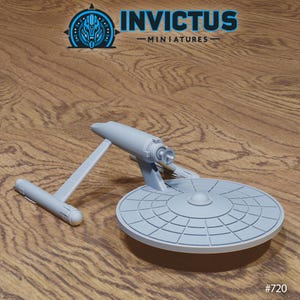 May include: A light grey miniature spaceship model with a circular main body and a long, thin secondary section. The model has detailed panel lines and is set against a wooden background. The Invictus Miniatures logo is visible.